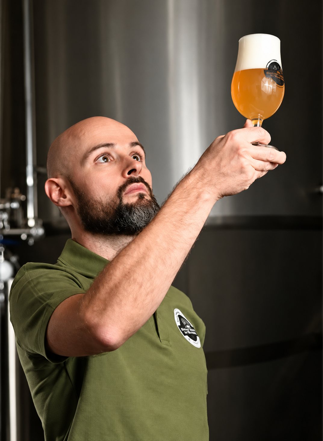 Un brasseur examine un verre de bière blonde devant les cuves