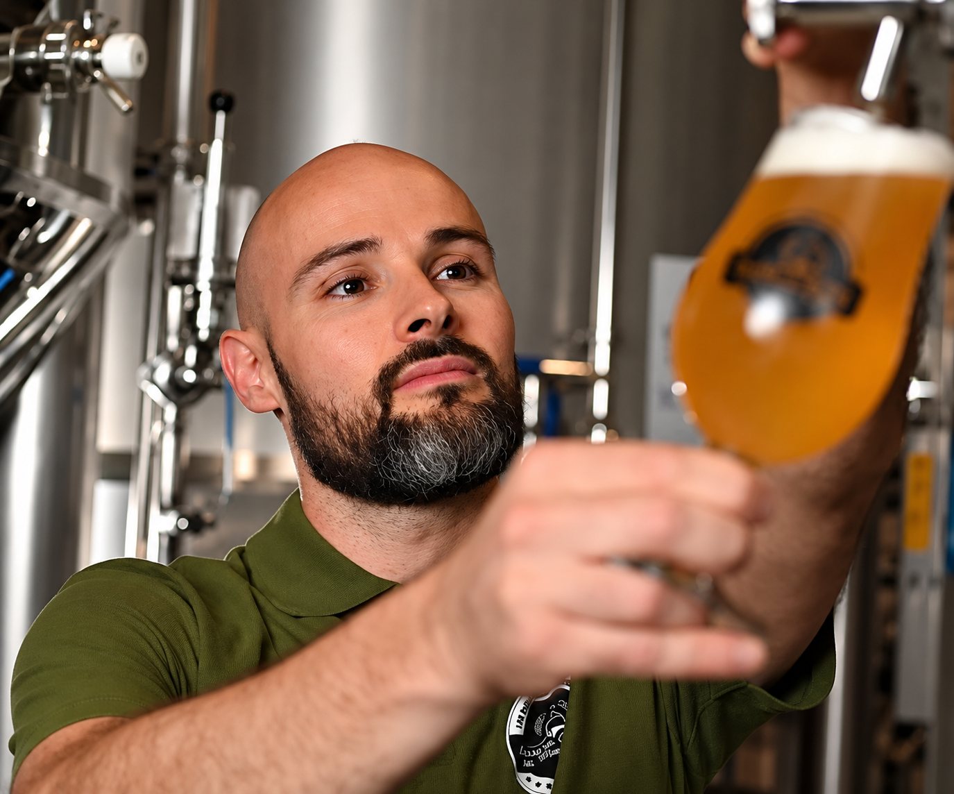 Un brasseur examine un verre de bière devant les cuves en inox