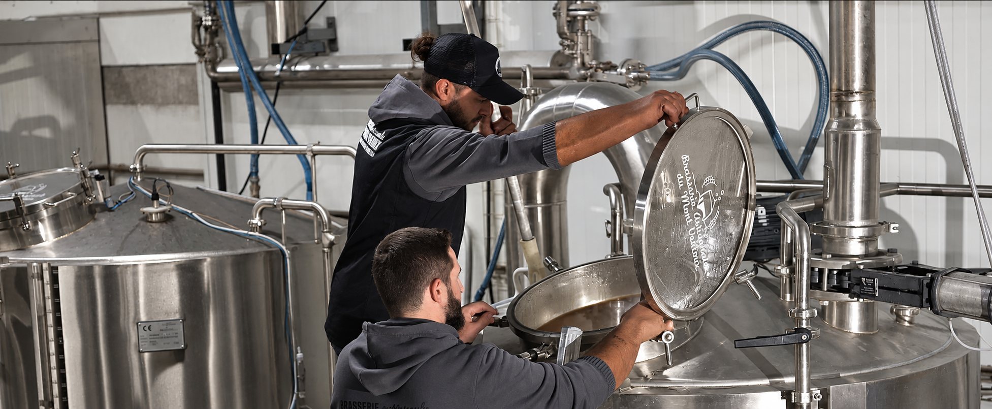 Deux brasseurs ouvrent la trappe d’une cuve de brassage en inox